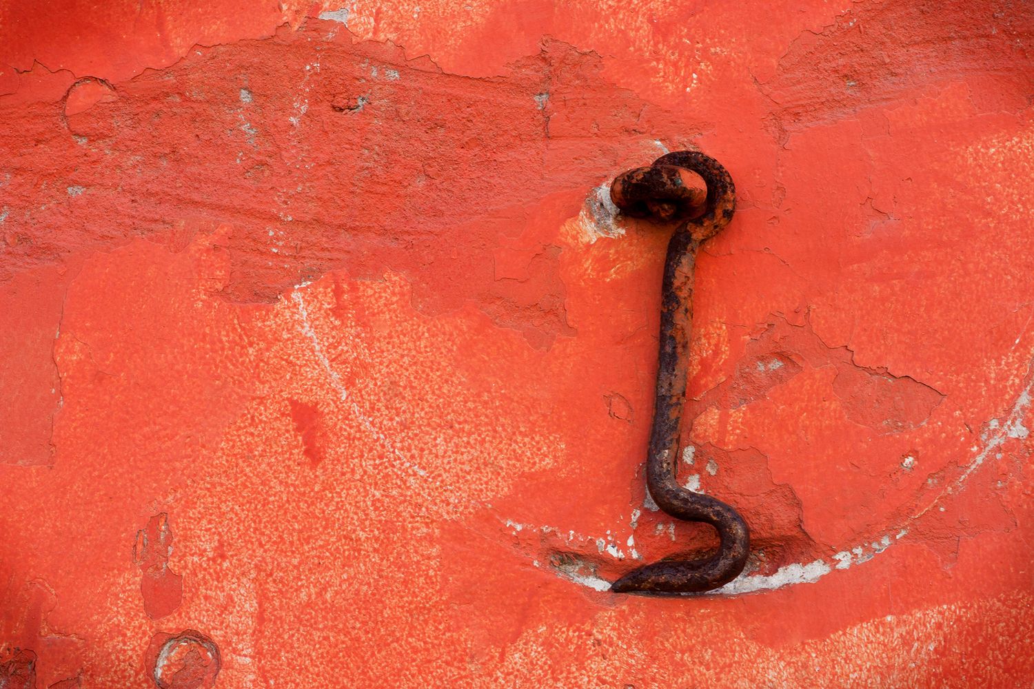 Rusty old hook mounted on weathered red painted metal surface.
