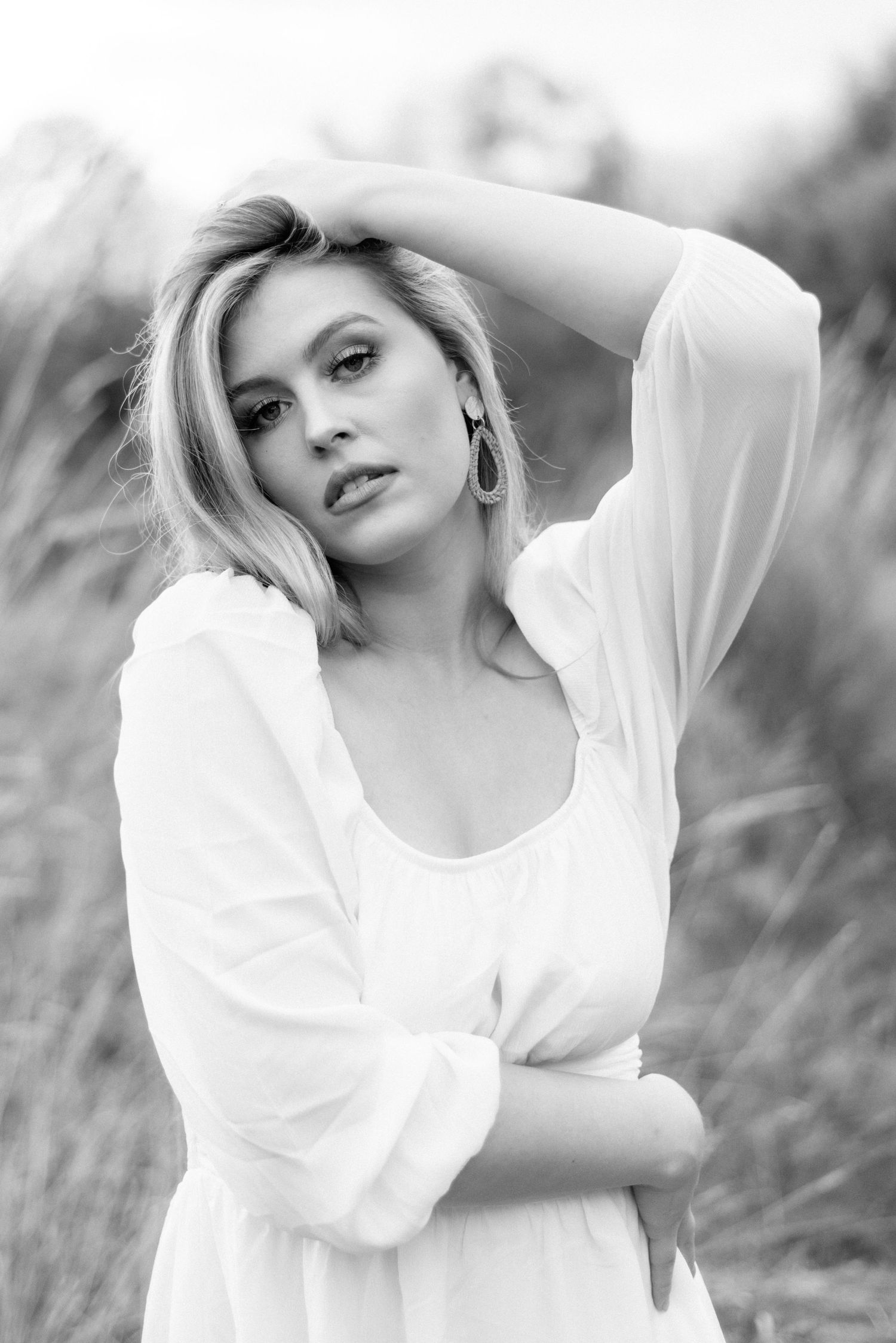 Black and white portrait in a dreamy white dress amidst natural outdoor scenery.