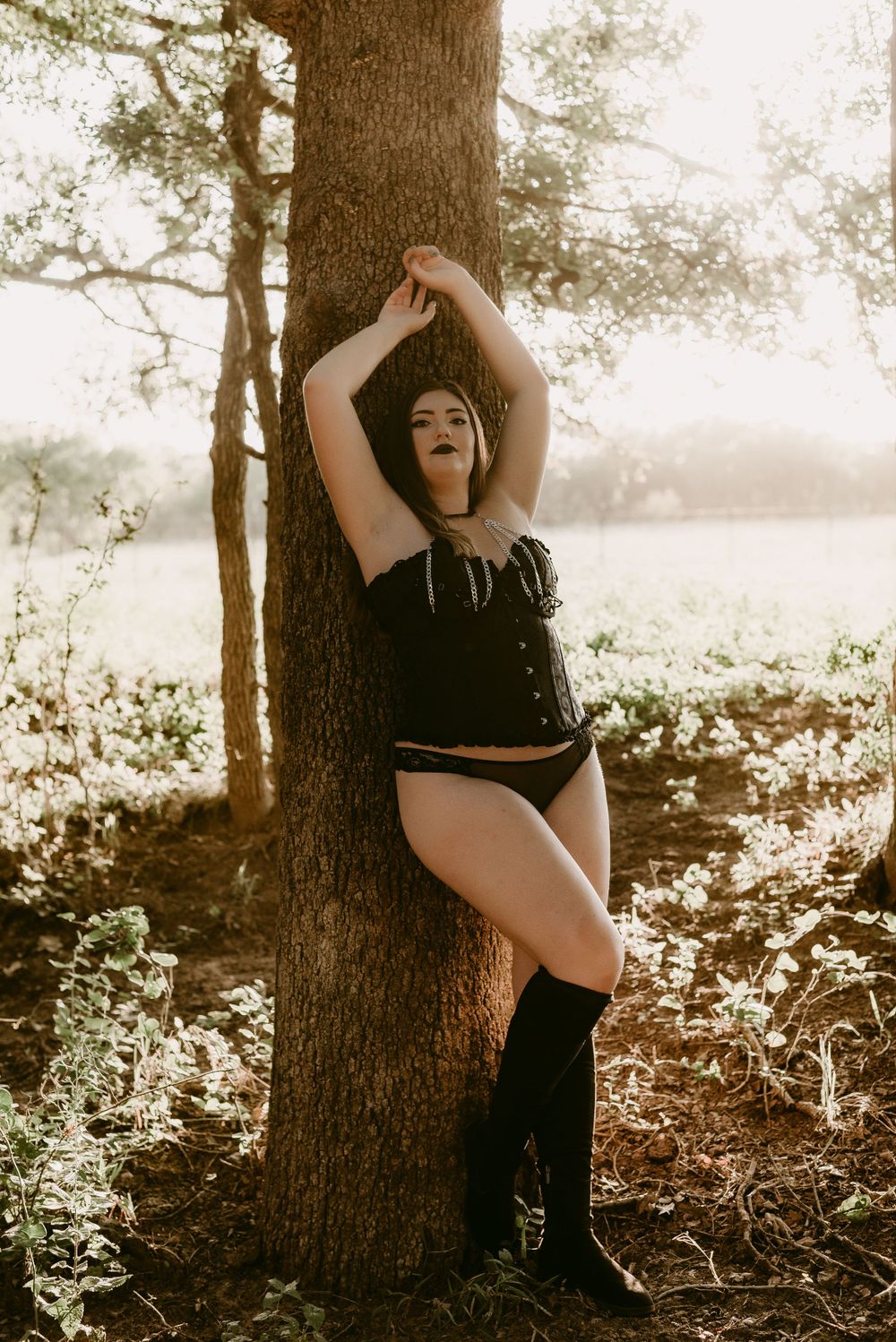 Vintage-inspired portrait against tree trunk with dramatic sunlit forest backdrop.