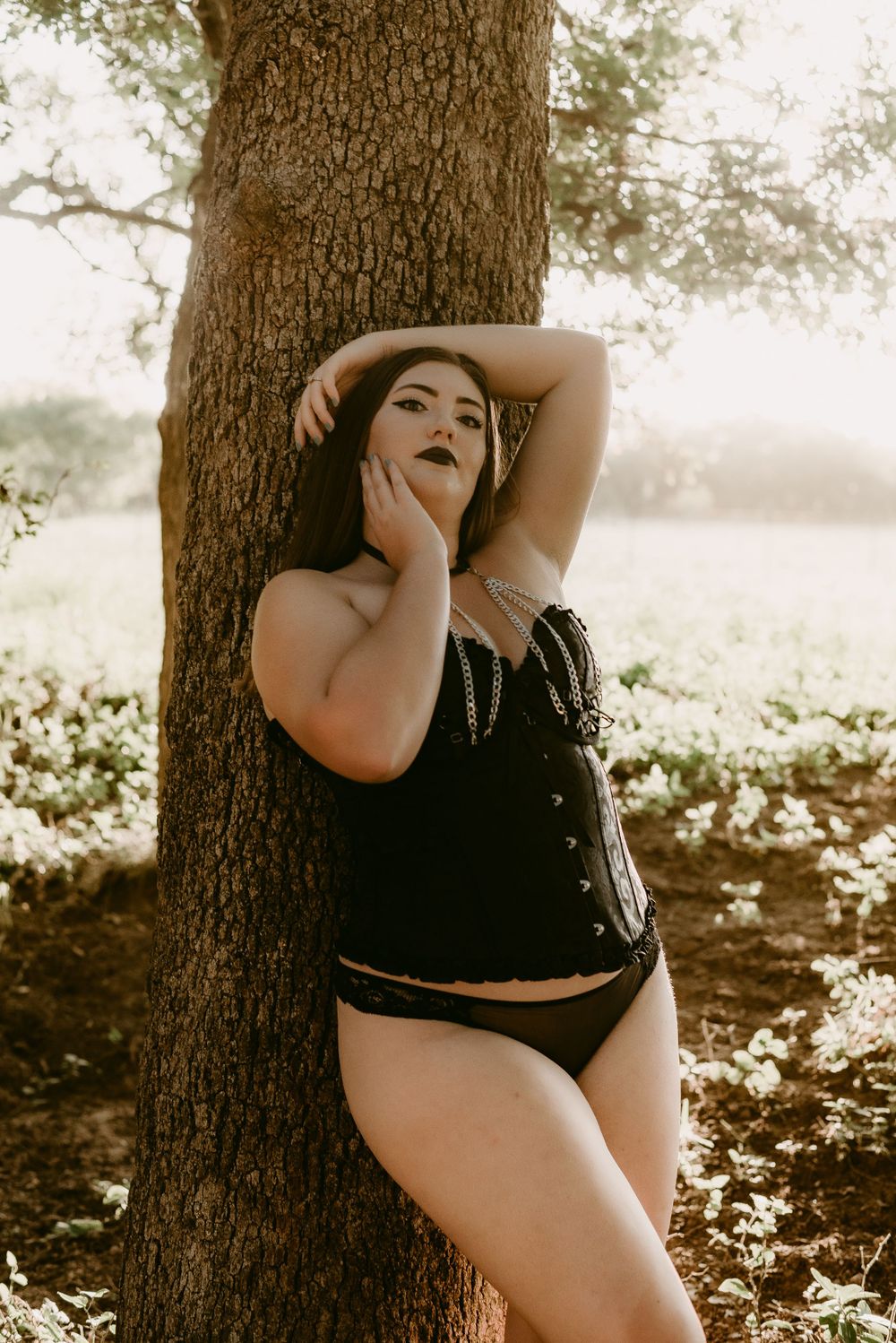 Artistic boudoir portrait against tree trunk in dreamy sepia tones.