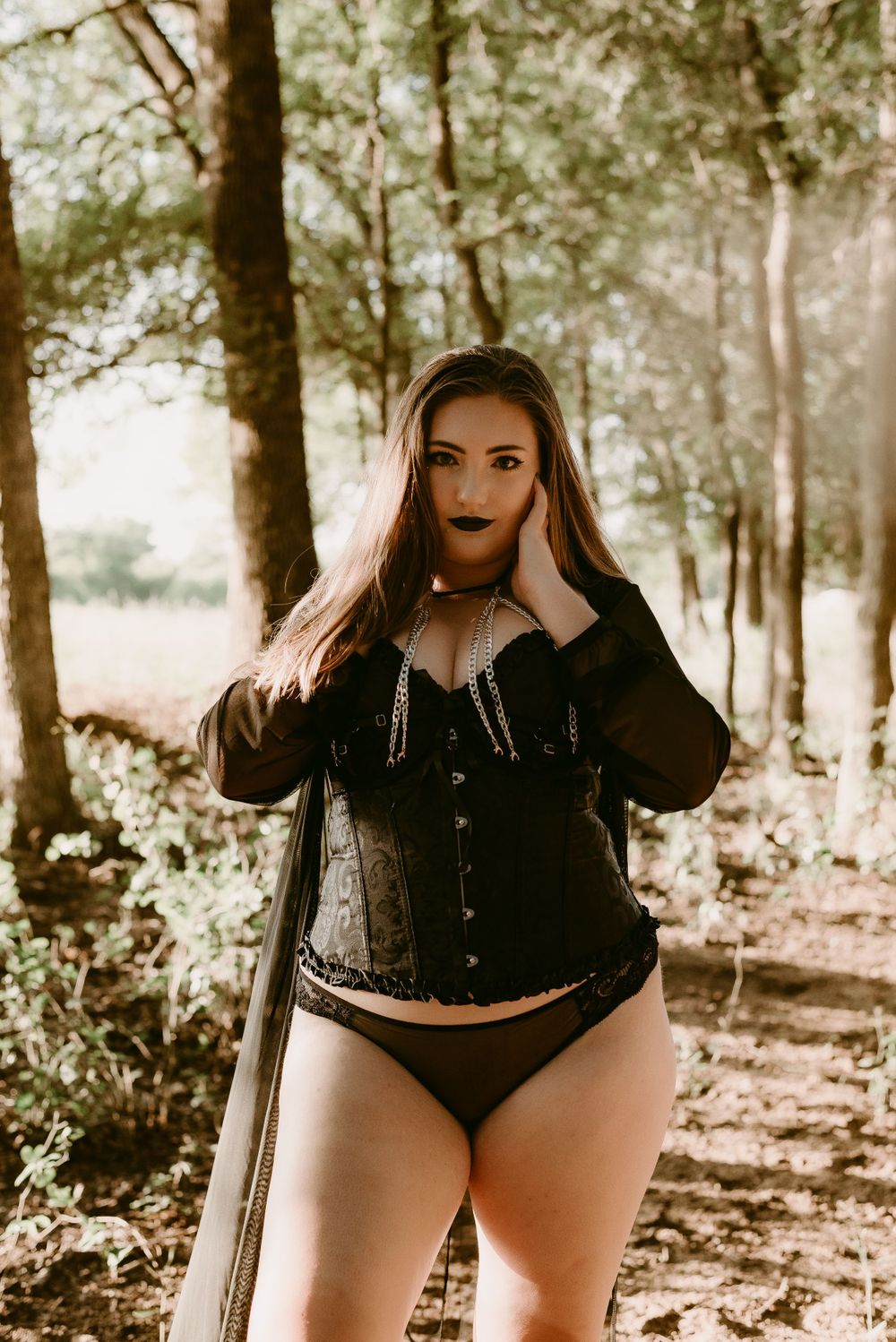 Boudoir photoshoot in a wooded setting featuring moody sepia tones and dark gothic fashion styling.