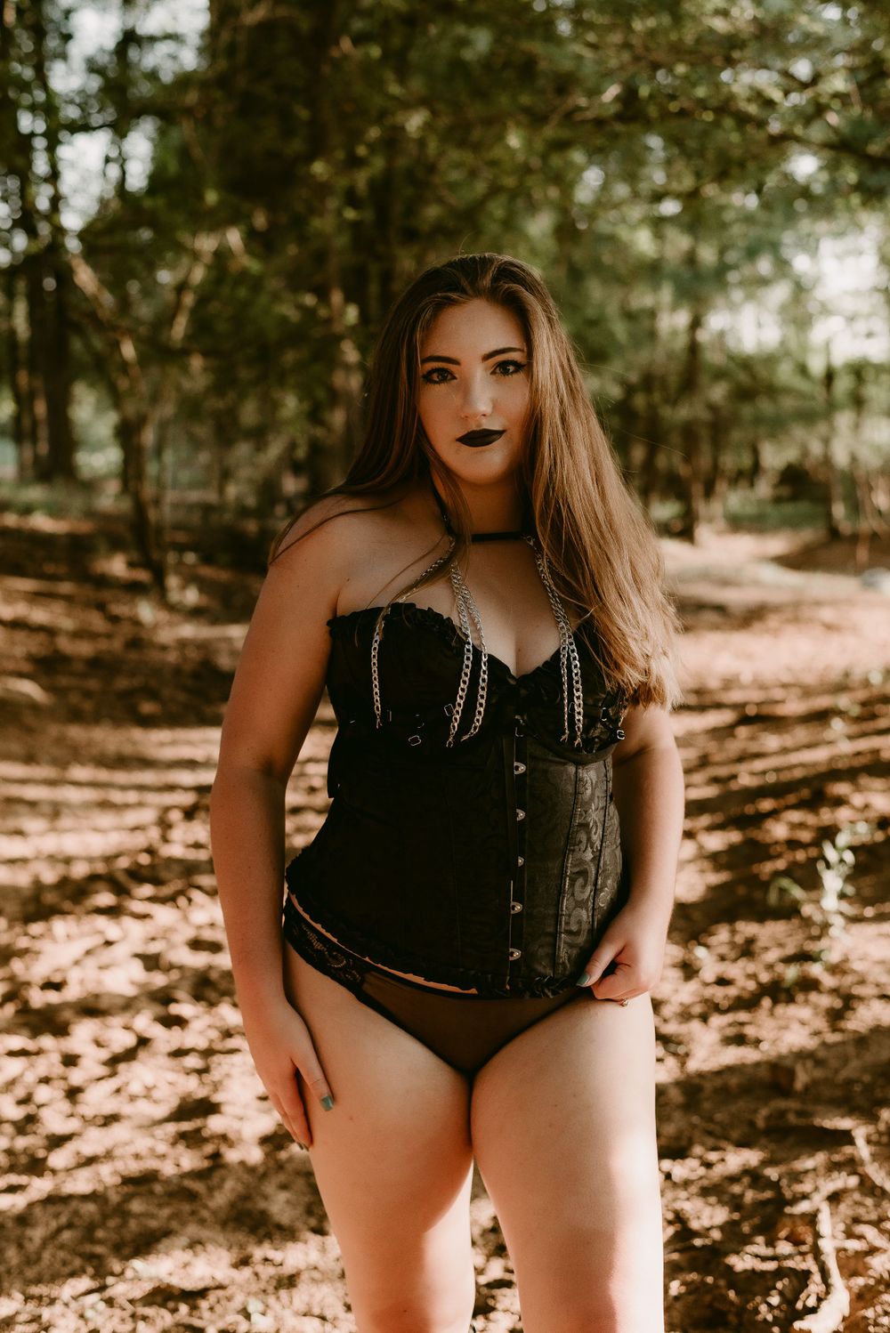 Alternative fashion portrait with corset styling photographed in dappled forest light.