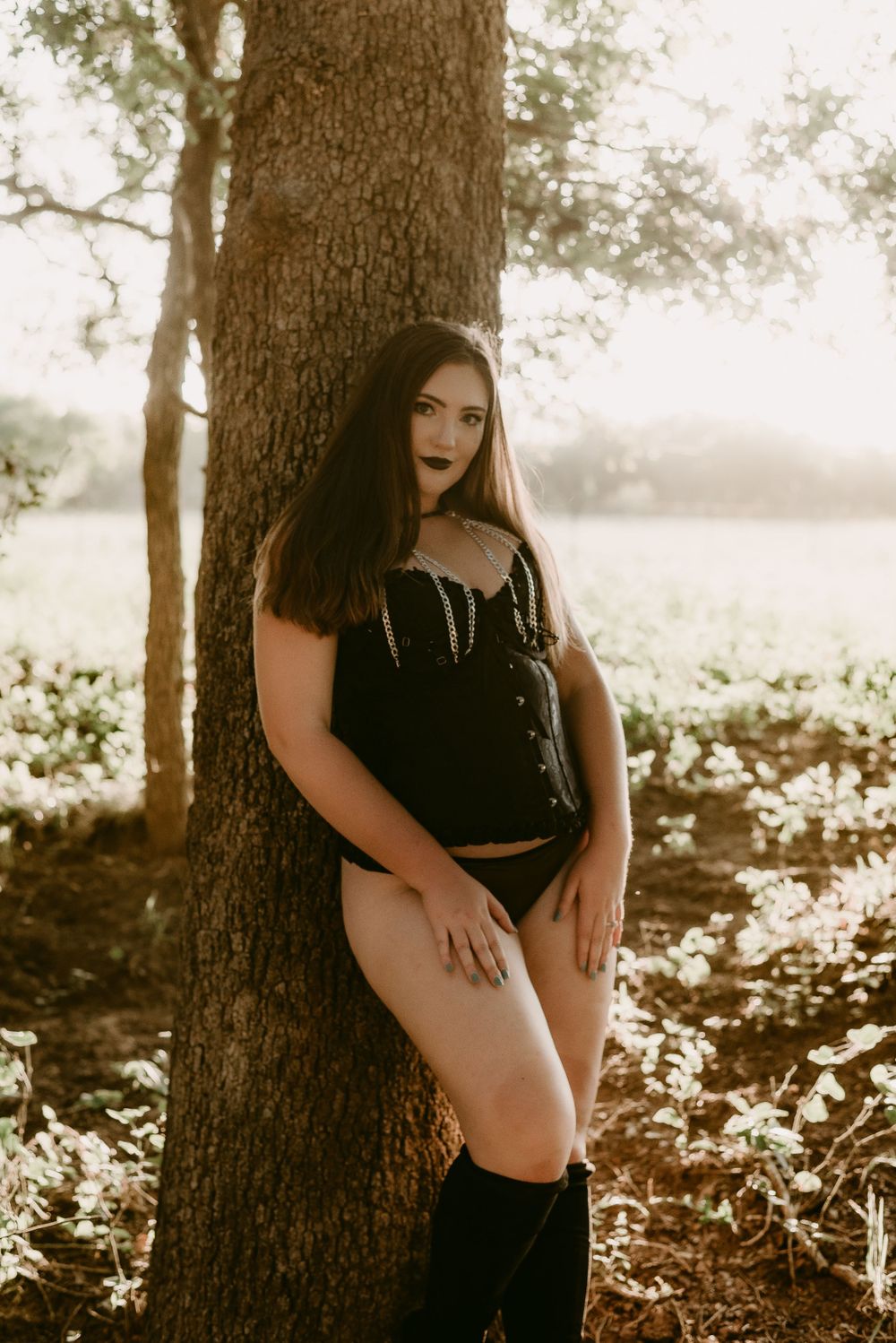 Atmospheric forest photoshoot featuring dark corset and tall boots in golden sunlight.
