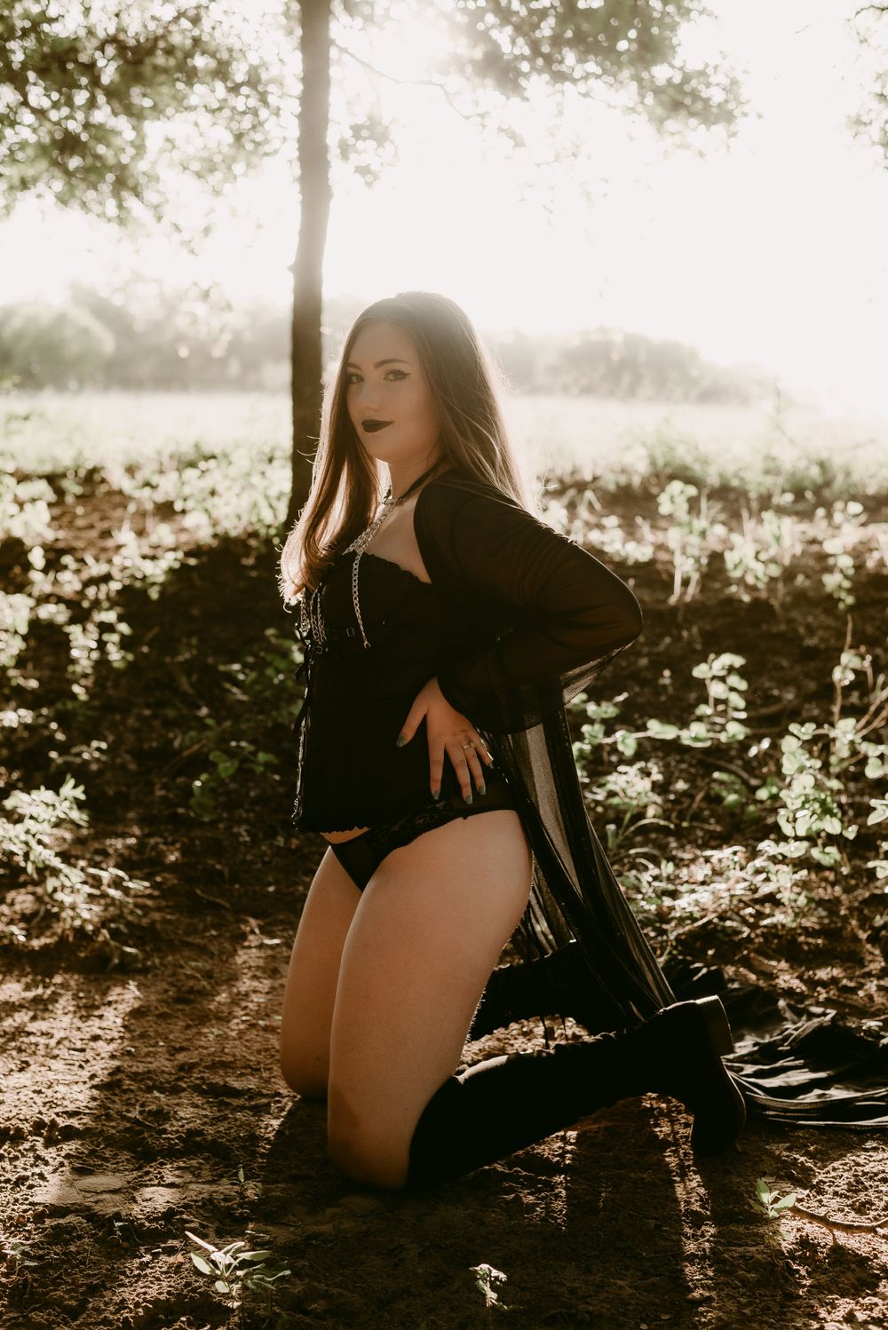 Artistic boudoir photography with backlit forest scenery and dark romantic aesthetic.