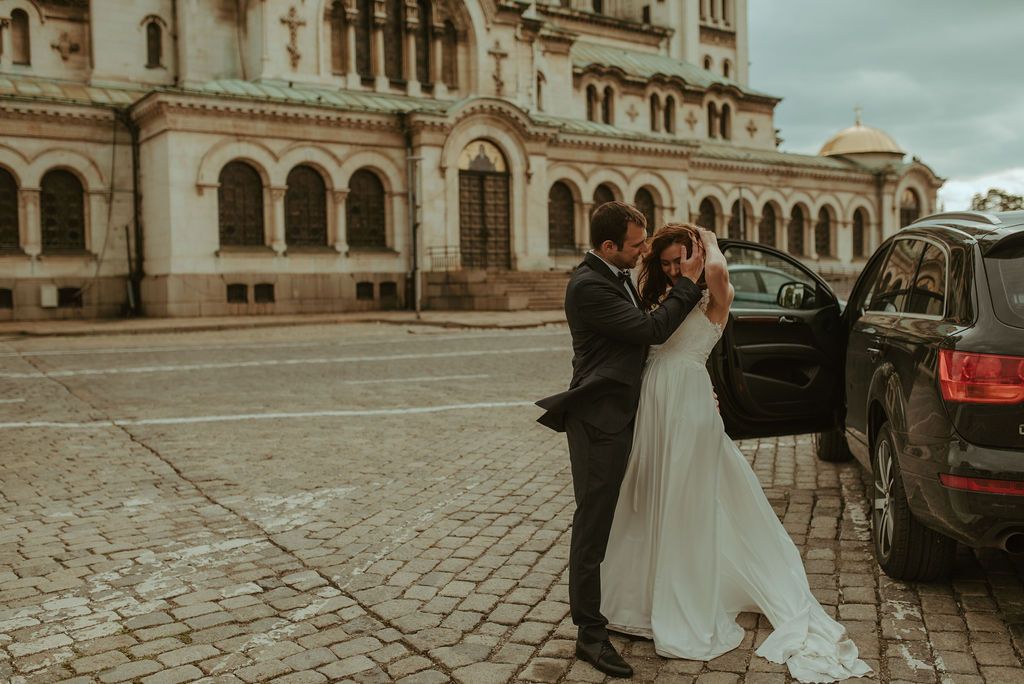 Wedding couple embracing outside historic building with classic architecture and cobblestone street.