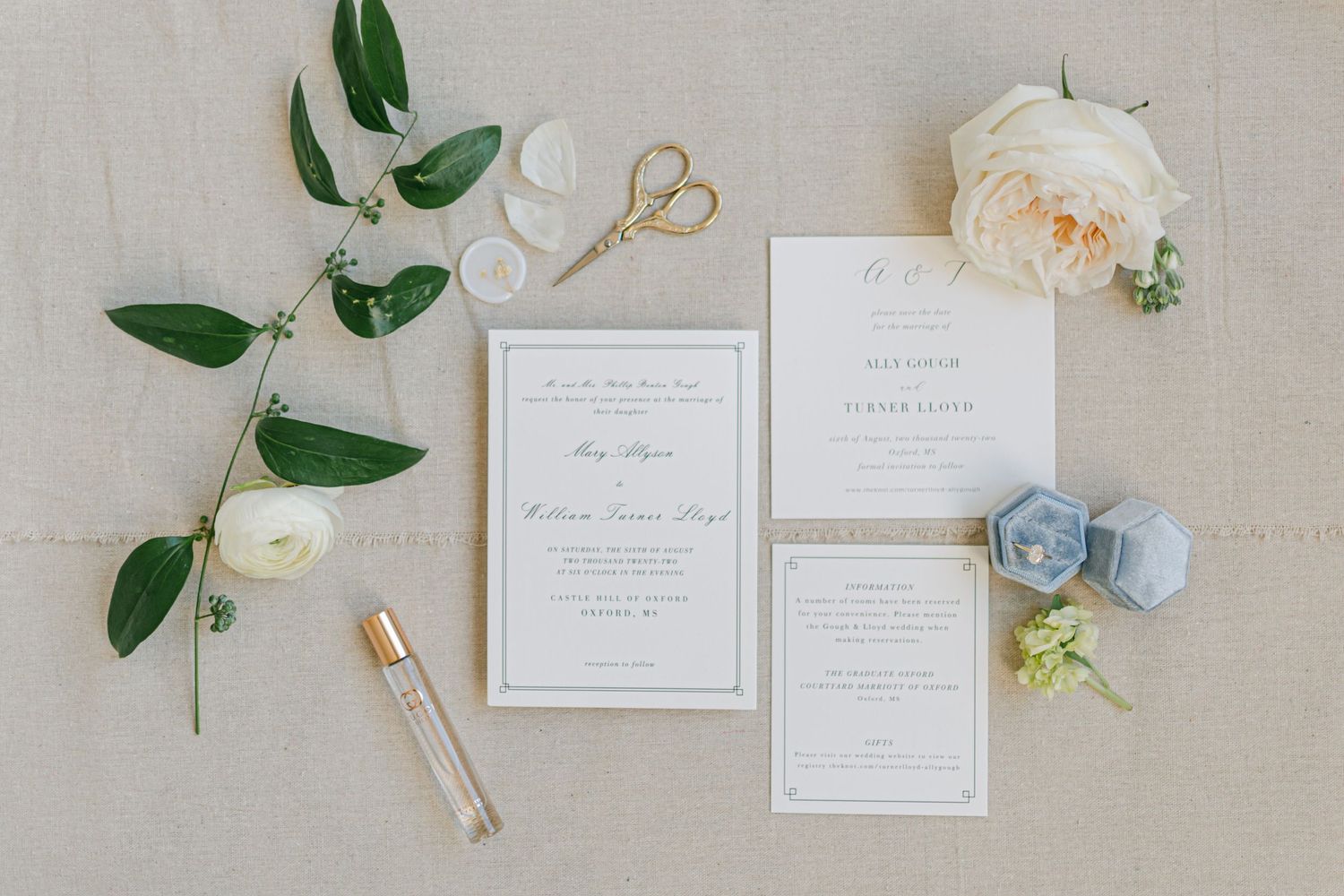 Elegant wedding invitation suite flat lay with white roses, greenery, blue ring box, and gold scissors.
