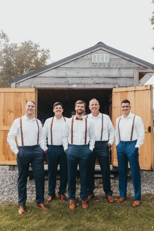 Group wearing matching navy pants and suspenders posing in front of a gray garage.
