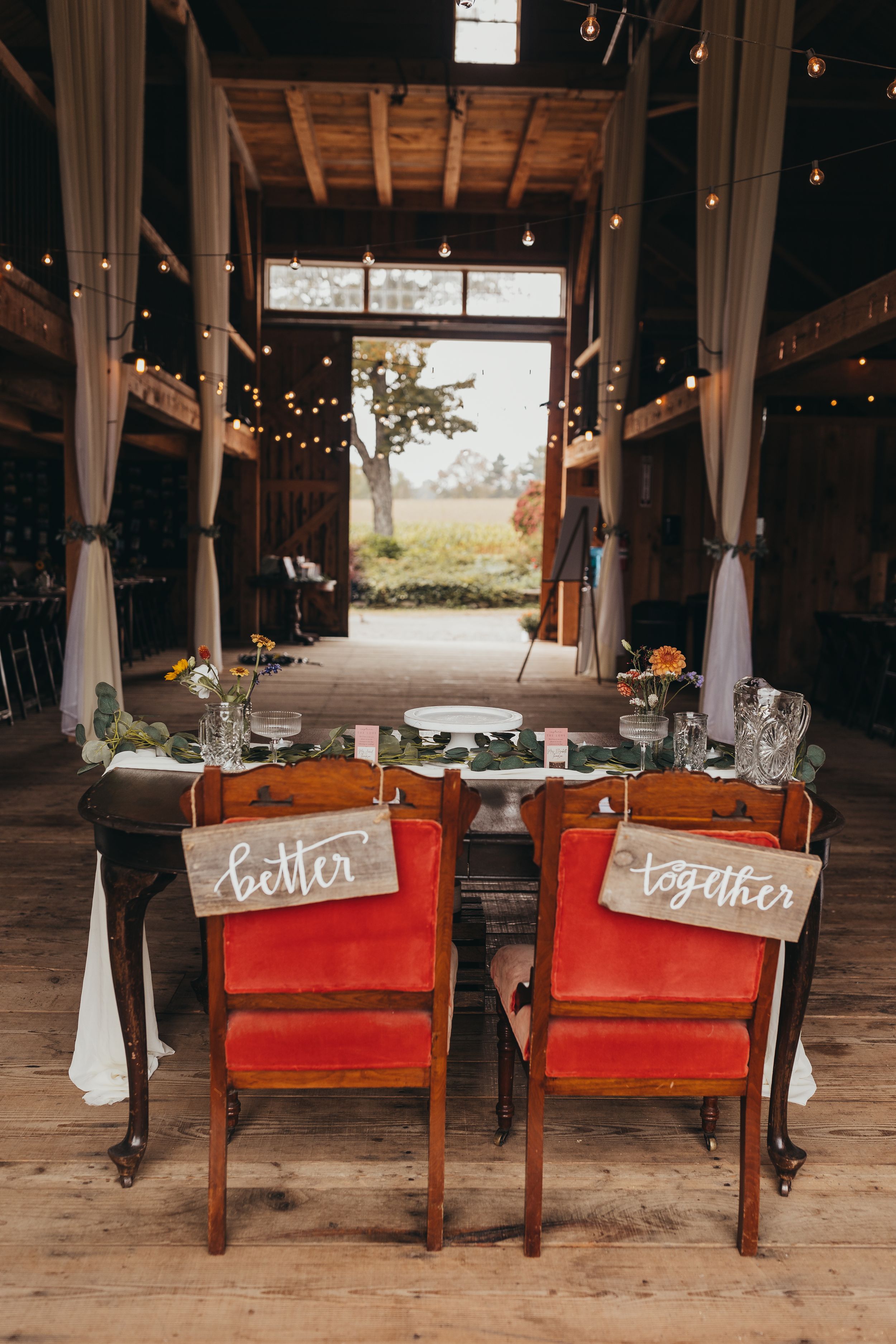 Vintage red church pews with handwritten signs in rustic barn venue.