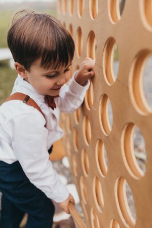 Young child in white shirt explores wooden decor at an outdoor event.