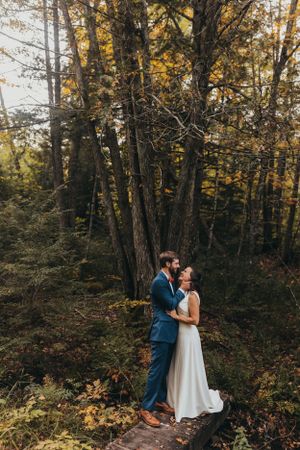 A couple shares an intimate moment in a wooded forest setting with golden autumn foliage.
