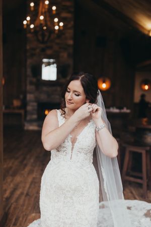 A bride adjusts her veil in an indoor venue with brick walls and ambient lighting.