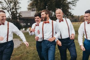 Group in coordinated outfits with suspenders laughing together outdoors.