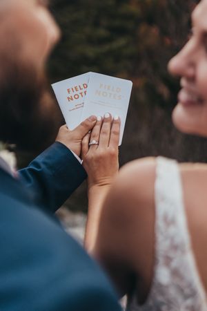 Close-up of hands holding Field Notes wedding vow books against blurred background.
