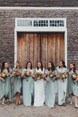 Wedding party in mint green dresses lined up against a rustic brick and wood backdrop.