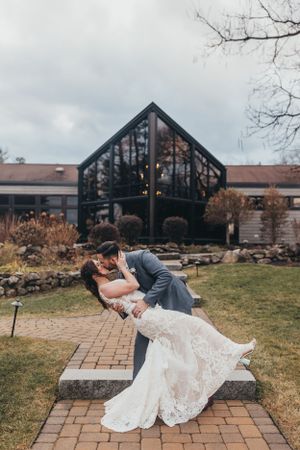 A dramatic dip pose between newlyweds on a brick pathway with a rustic building backdrop.