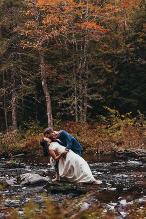 A dramatic dip pose captured against a backdrop of autumn trees and flowing water.