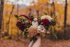 Autumn floral arrangement with pink and burgundy blooms against fall foliage backdrop.