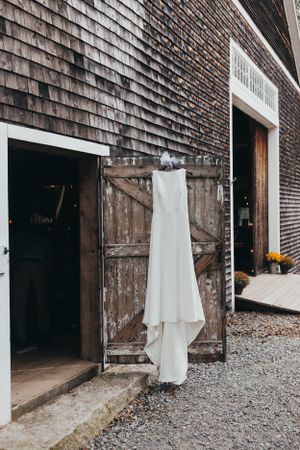 White dresses hanging outside rustic wooden barn doors with gravel pathway.