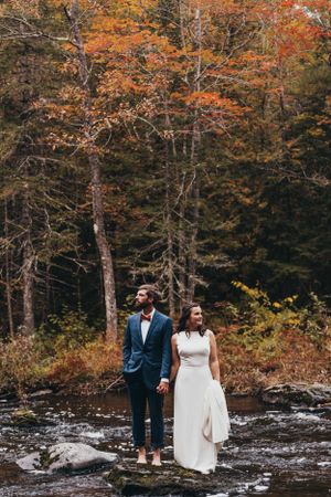 A romantic scene unfolds by a rushing stream surrounded by vibrant fall colors in the forest.