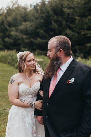 Bride and groom in formal attire share candid moments outdoors.