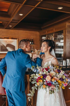 A couple shares champagne at their wedding reception in an elegant wood-paneled bar.