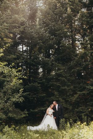 Wedding couple shares intimate moment among lush green forest trees.