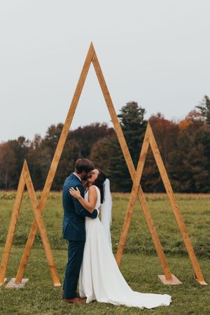 Couple shares intimate moment in front of geometric wooden backdrop during outdoor wedding ceremony.