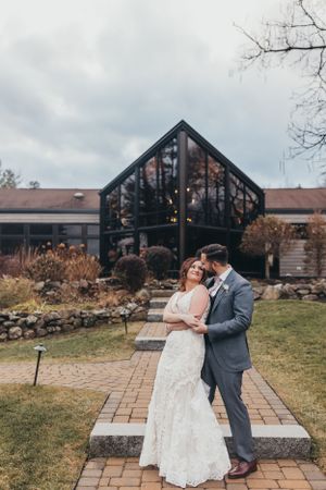 A couple shares an intimate moment outside a modern chapel building.
