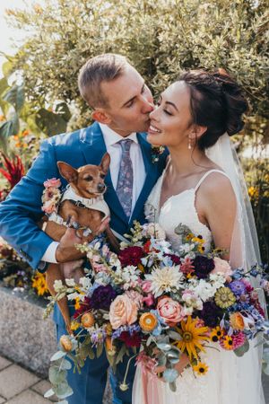 A couple with their small dog poses with a vibrant wildflower bouquet on their wedding day.