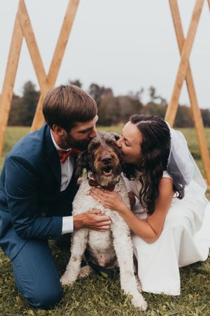 Newlyweds share joyful moment with their fluffy white dog in grassy field.