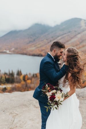 Romantic wedding couple embraces against a backdrop of misty mountains and autumn foliage.
