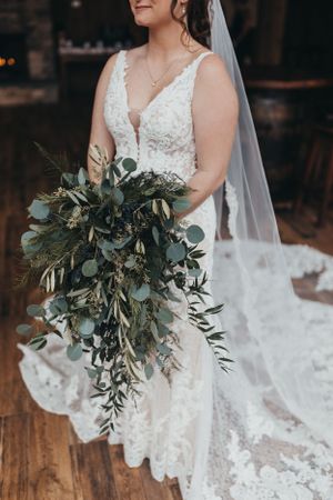 Close-up of a lush greenery and eucalyptus wedding bouquet against a white lace wedding dress.