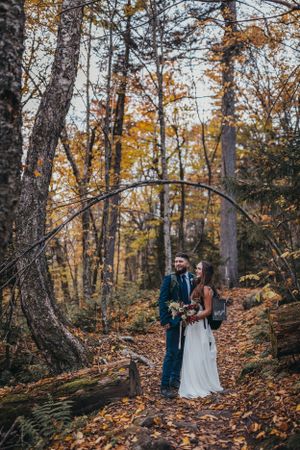 Couple walking through autumn forest with fallen leaves on ground.