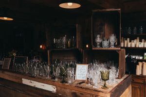 Vintage glassware and bottles displayed on wooden shelves in dimly lit bar setting.
