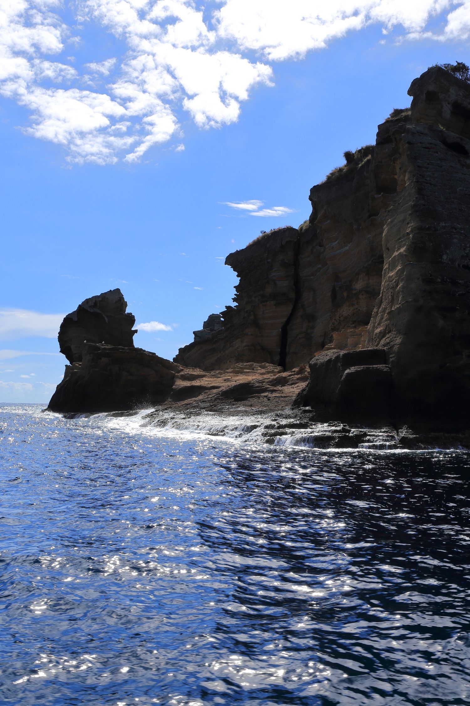 Rugged sea cliffs rise dramatically from sparkling blue waters under bright sunlight.
