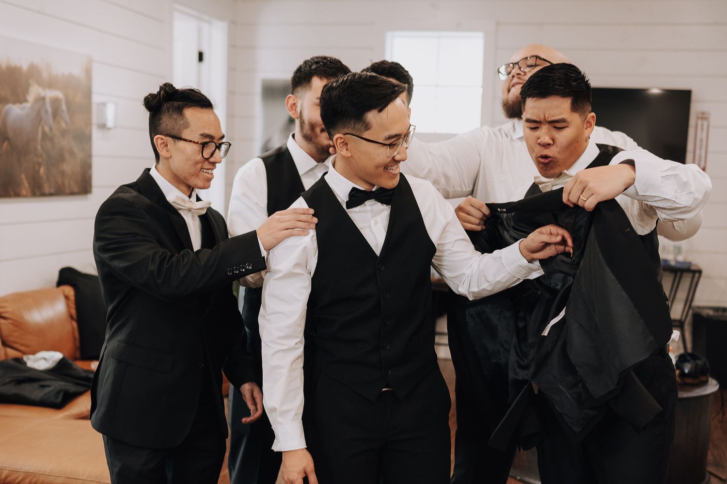 Groomsmen in black tuxedos help adjust each other's formal attire before the ceremony.