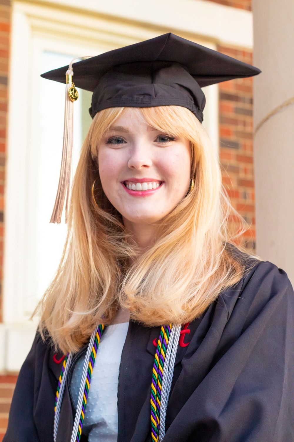 A grad wearing her grad gown, tassel, and cap smiling at the camera.
