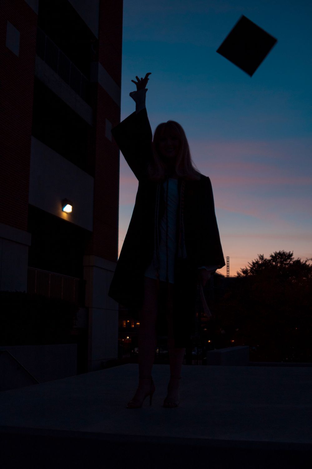 A grad throwing her cap while the sun is setting.