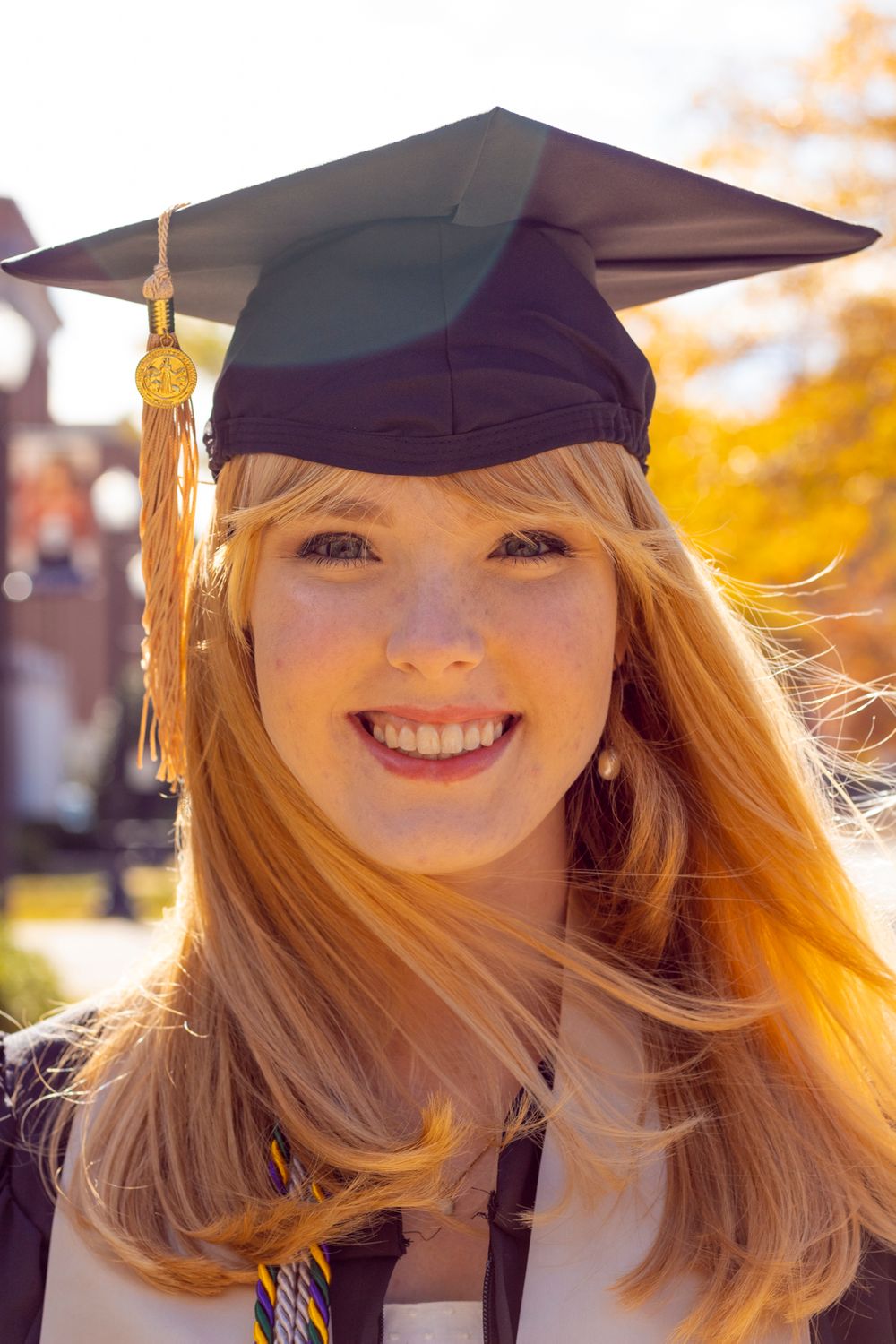 A grad wearing her grad gown, stole, tassel, and cap smiling at the camera.
