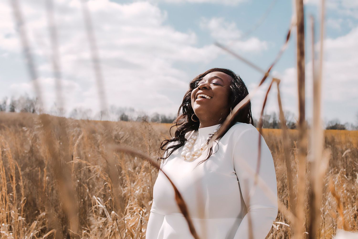 Woman in white sweater enjoying a sunny day in a golden wheat field.
