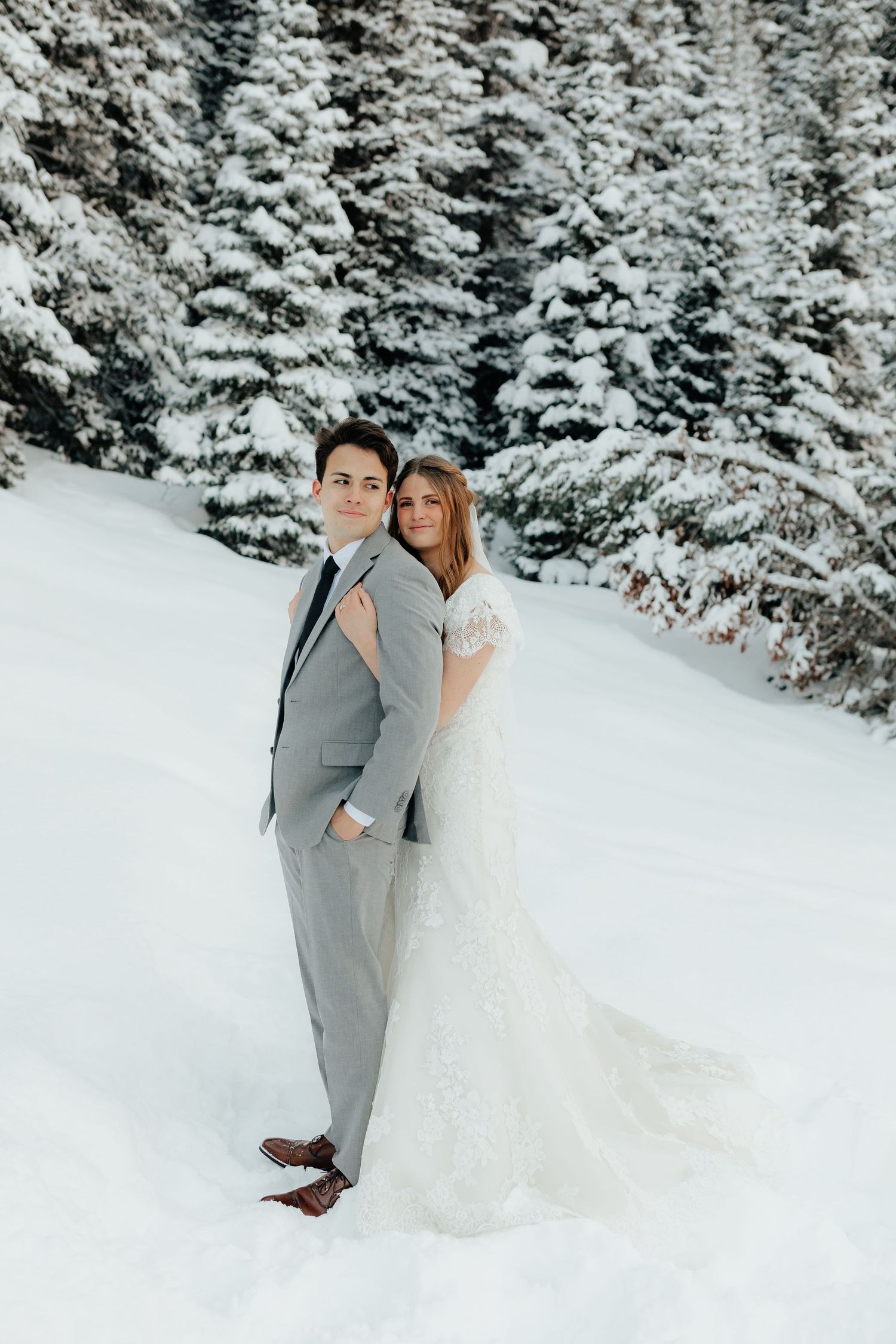 Bride hugging groom from behind in winter pine forest