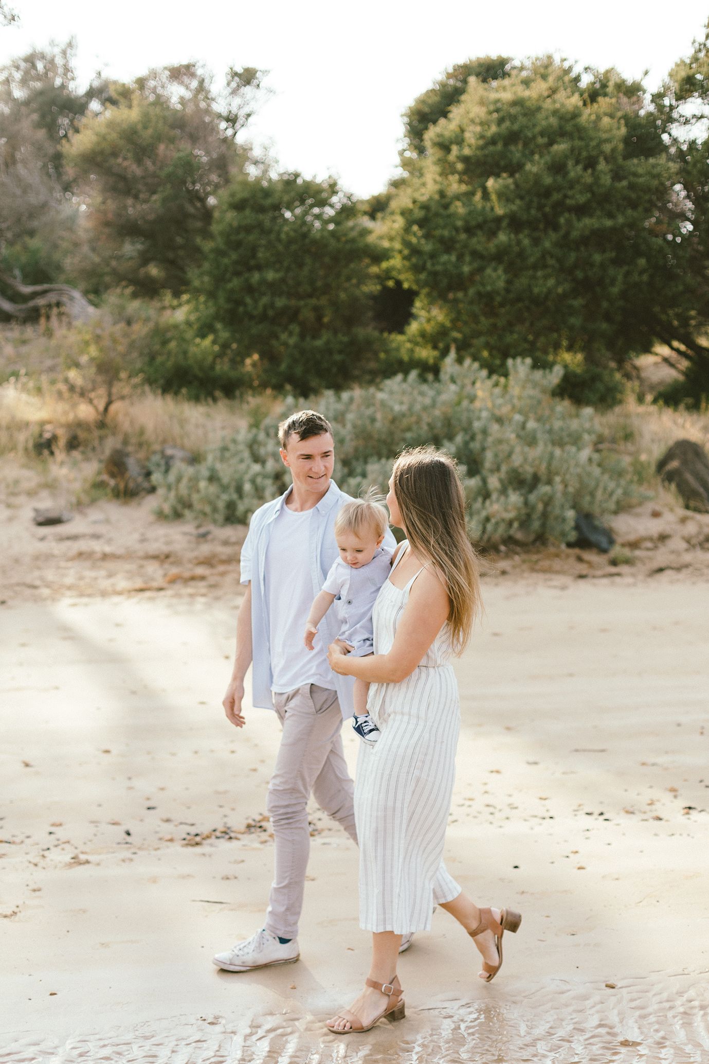 A family in coordinating white outfits walks together on a sandy beach.