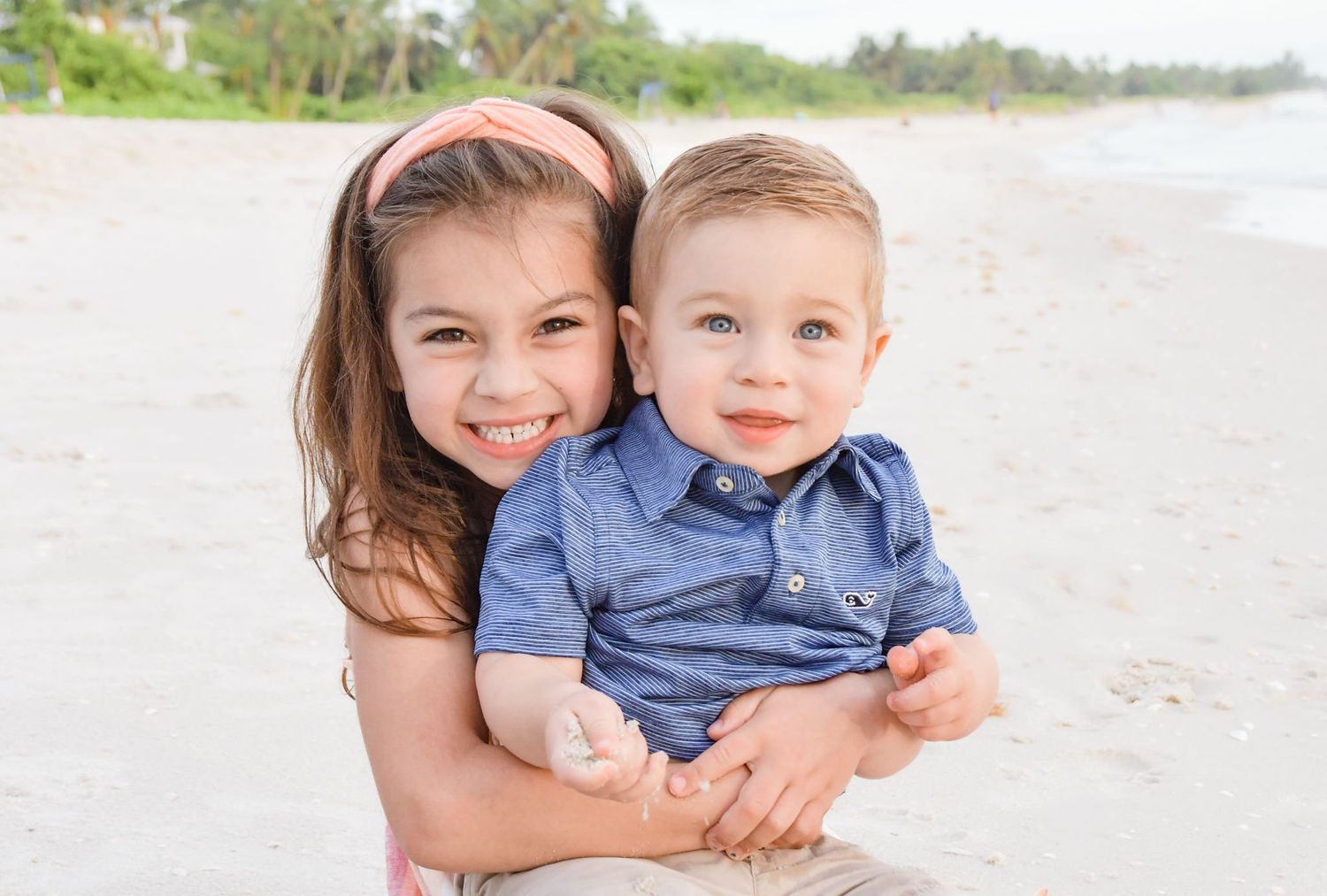 Two children smiling together on sunny beach.