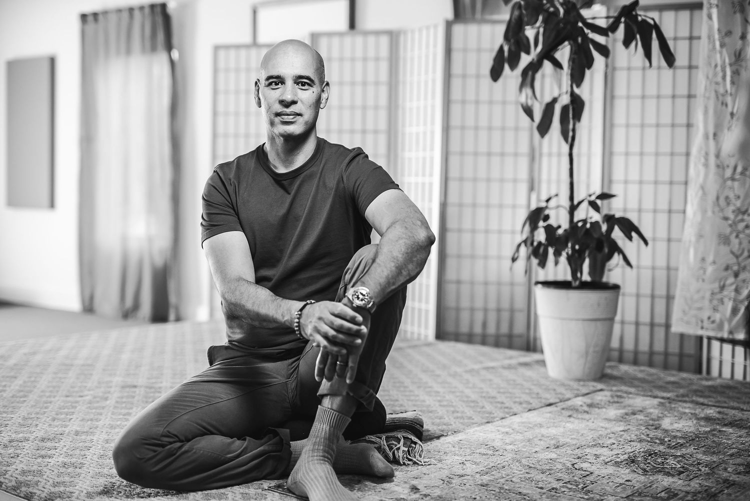 Black and white portrait of someone sitting casually on a floor next to a potted plant.