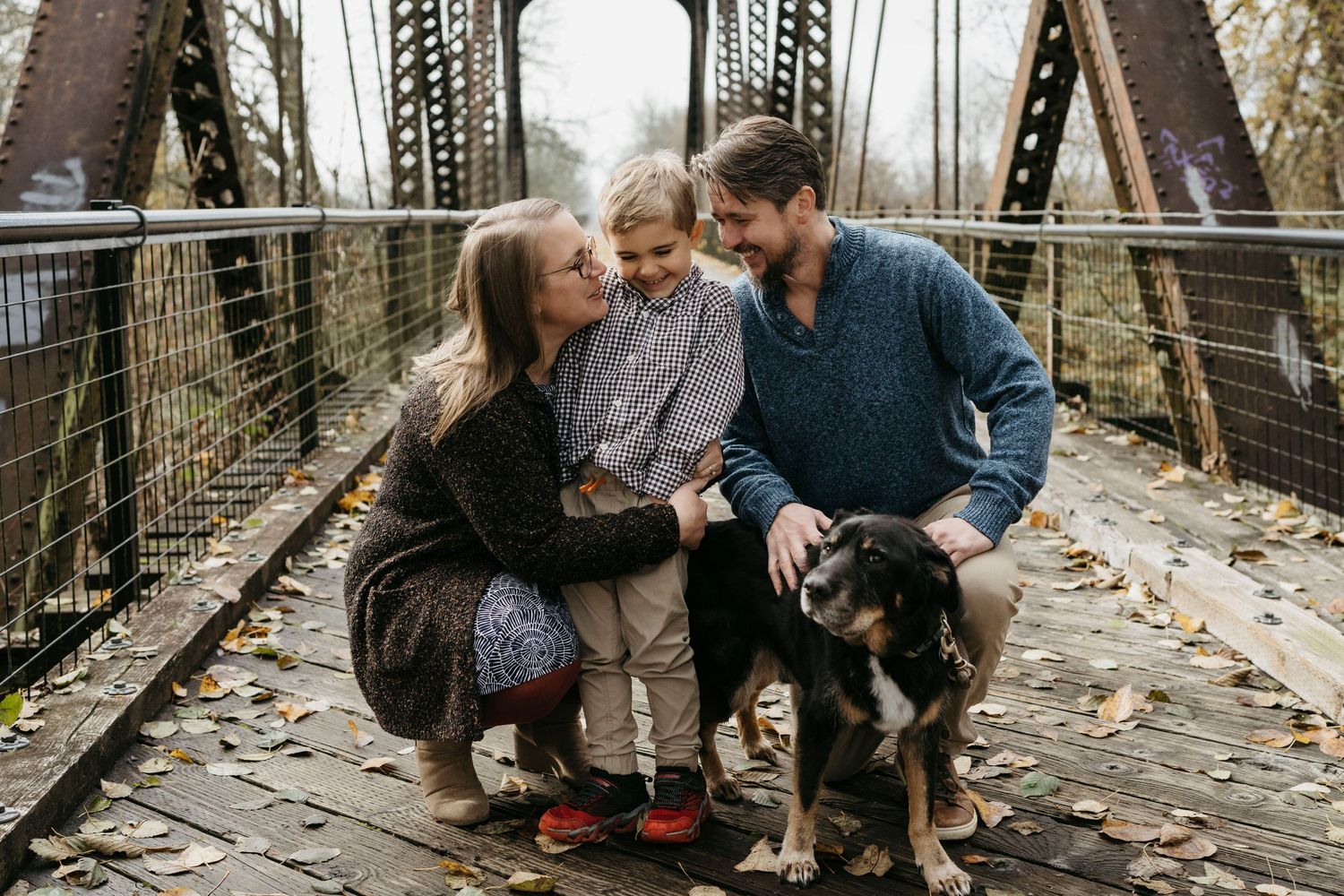 Family enjoying a moment together with their dog on a rustic bridge.