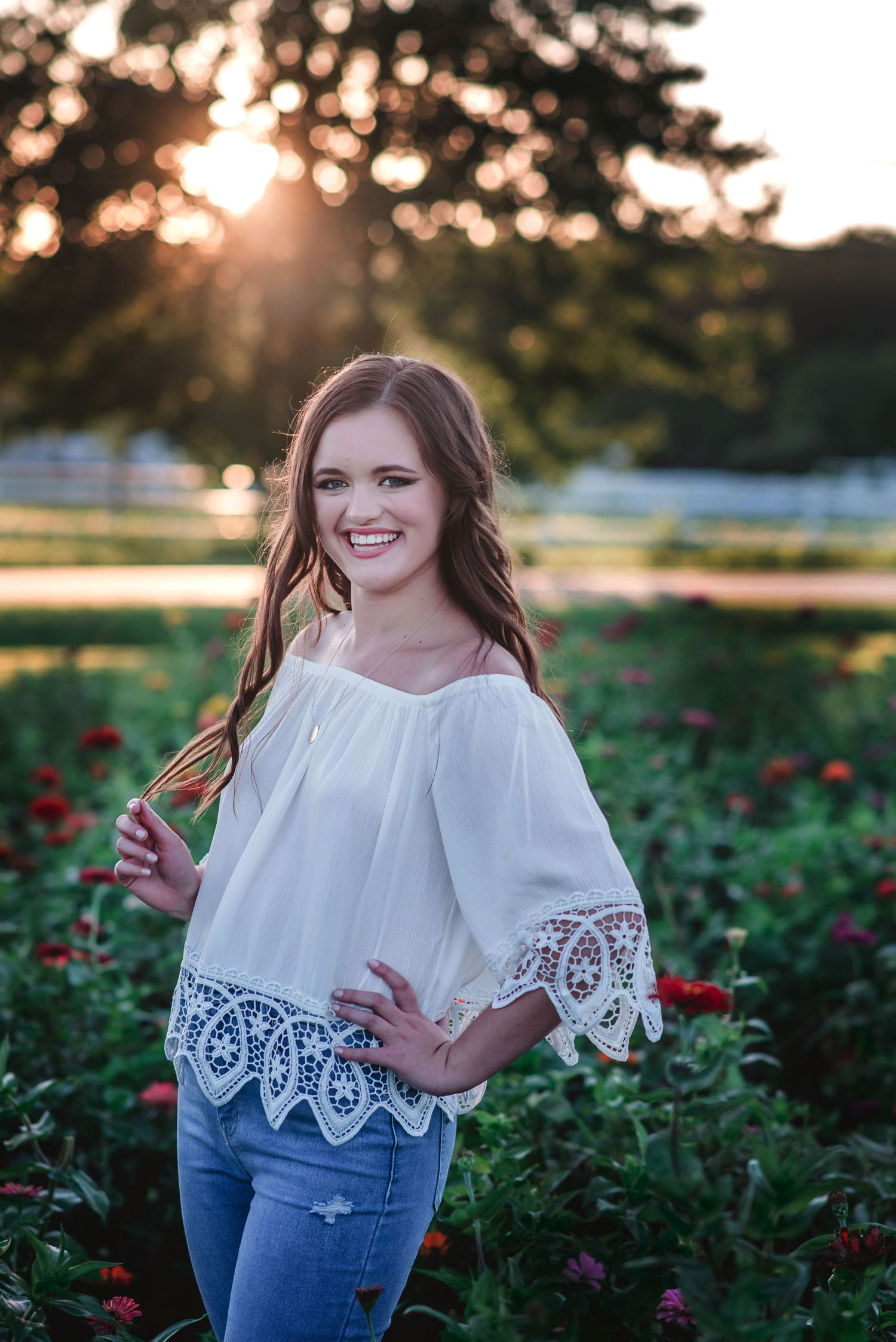 a photo of a smiling high school senior girl standing in a flower field