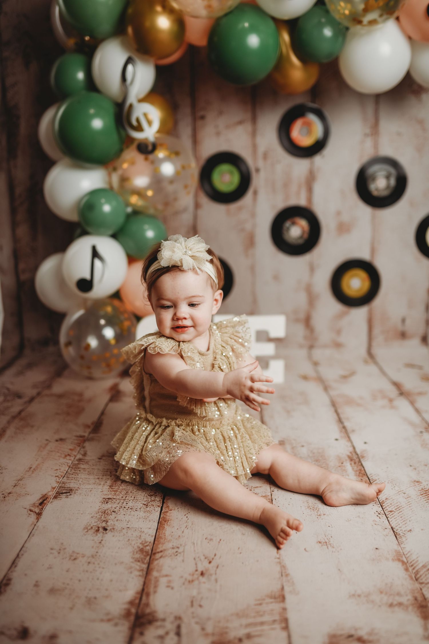 Festive setup with green and gold balloons and vinyl records on wall for special occasion photo shoot.