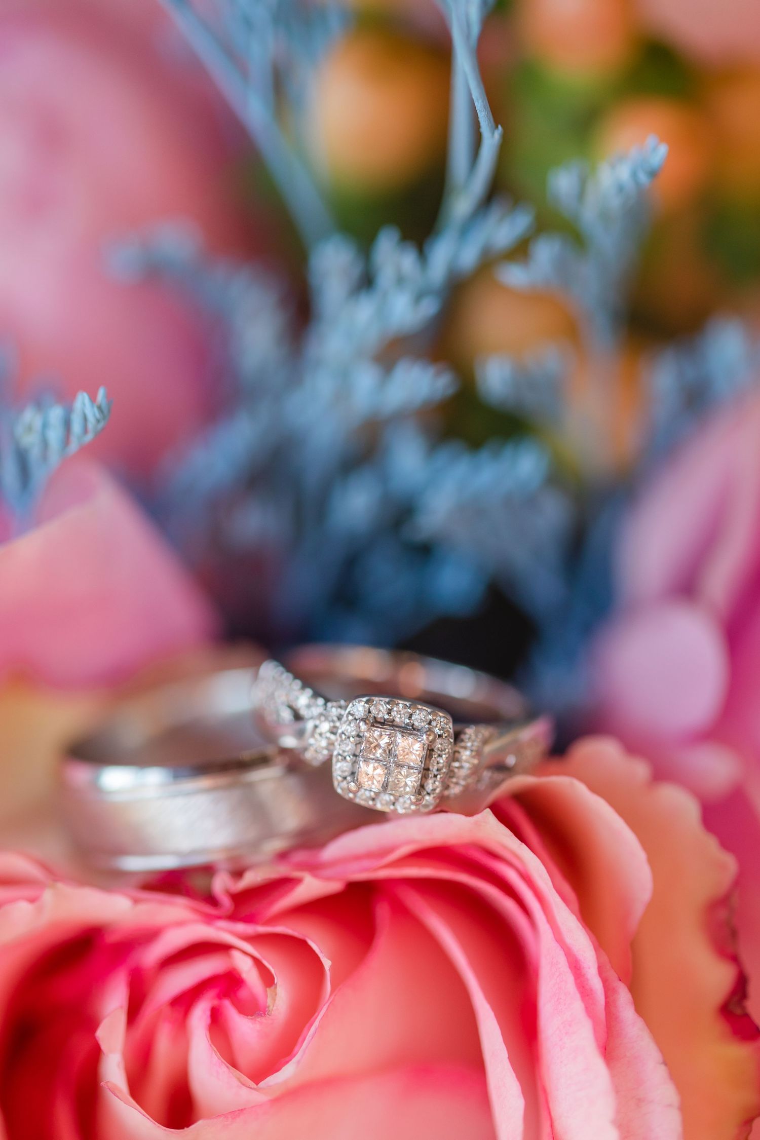 Diamond engagement ring nestled on pink rose petals with blue flowers.