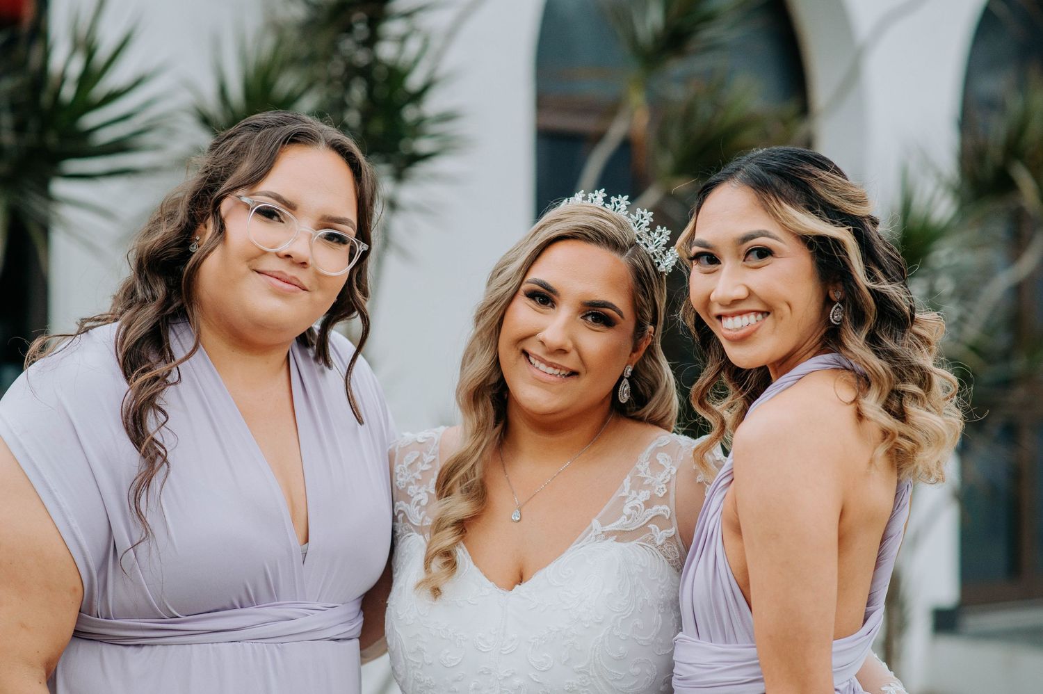 Three women pose together at a wedding wearing light purple bridesmaid dresses.
