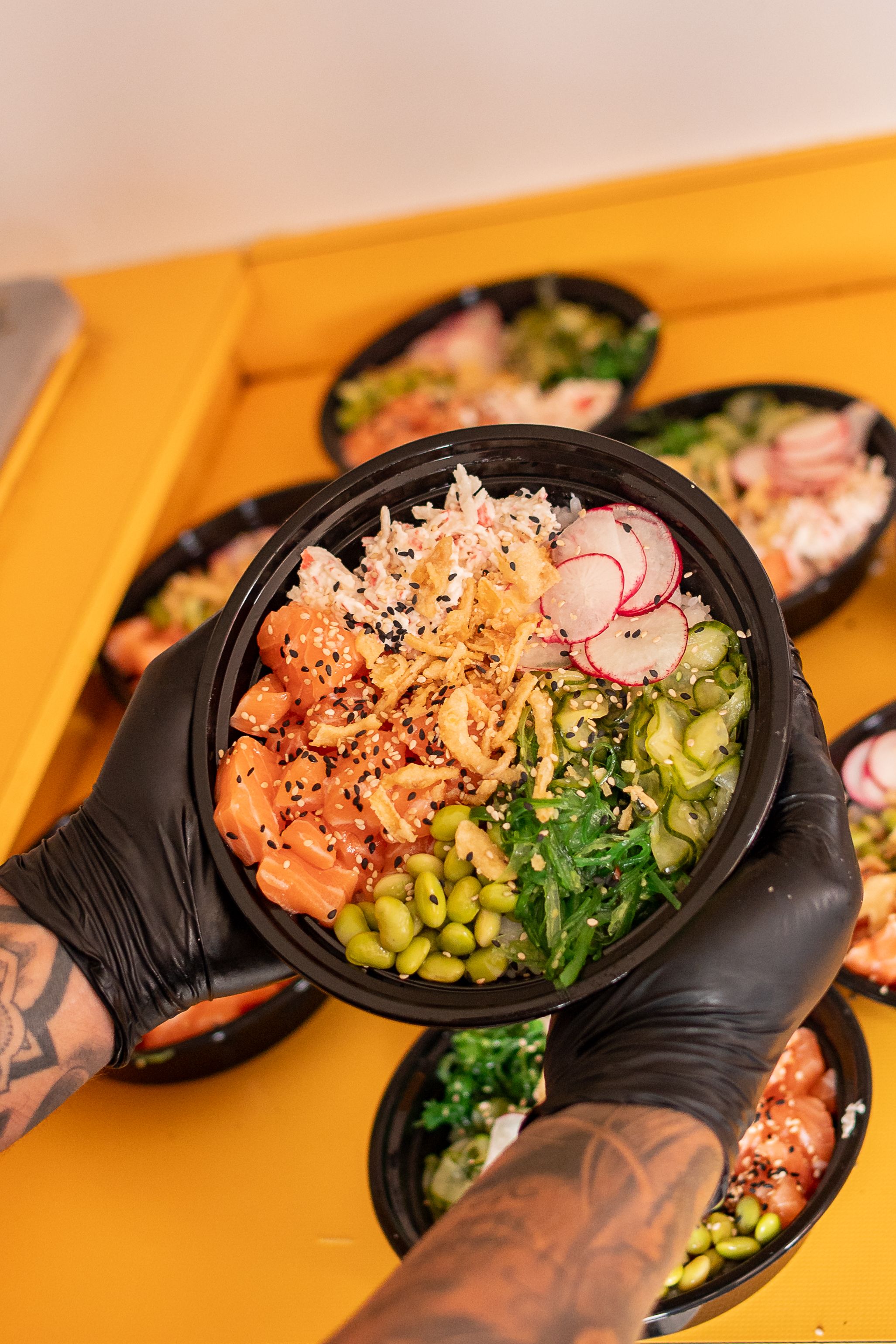 Tattooed hands serving colorful poke bowl with fresh salmon, radishes and greens.